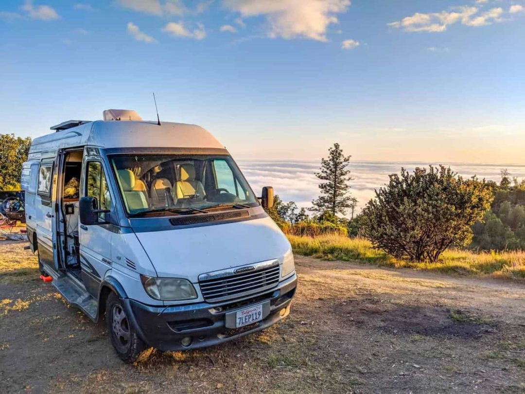 Van parked in a camp spot with a beautiful view of clouds and a sunset behind it