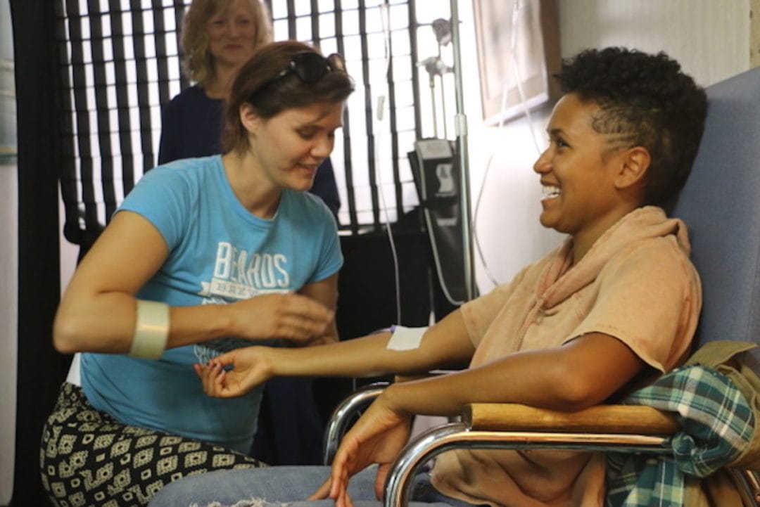 Emily Manthei lays a fake chemo IV on an actor's arm.