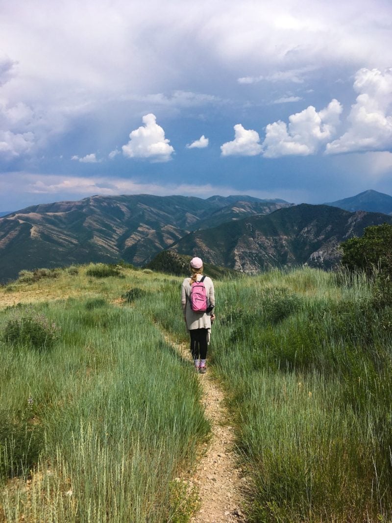 Allen stands alone on a path in front of a large mountain range.
