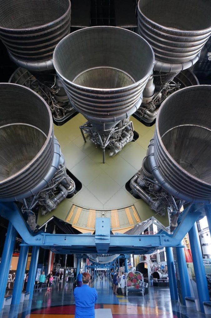 an individual stands under the giant engines of the saturn v