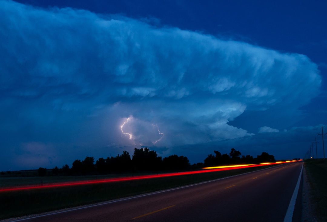 traffic lights blur at night as a storm rages in the distance
