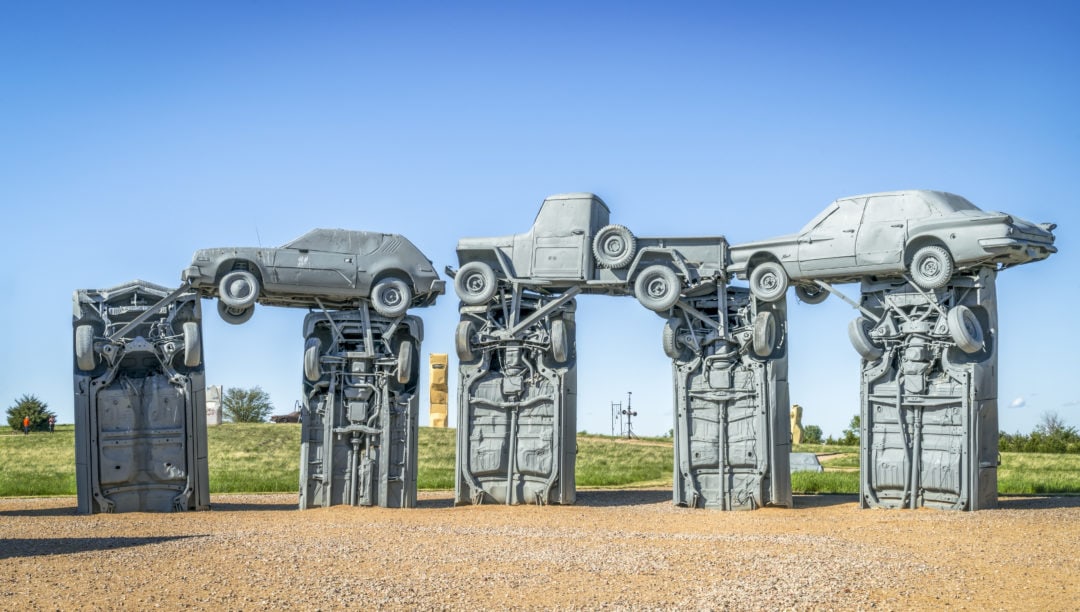 A group of silver-painted cars are stacked on top of each other in an effort to resemble Stonehenge 