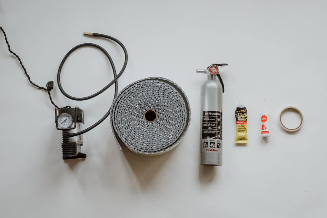 Shot of various RV essential items, including tire pressure gauge, fire extinguisher, glue and tape.
