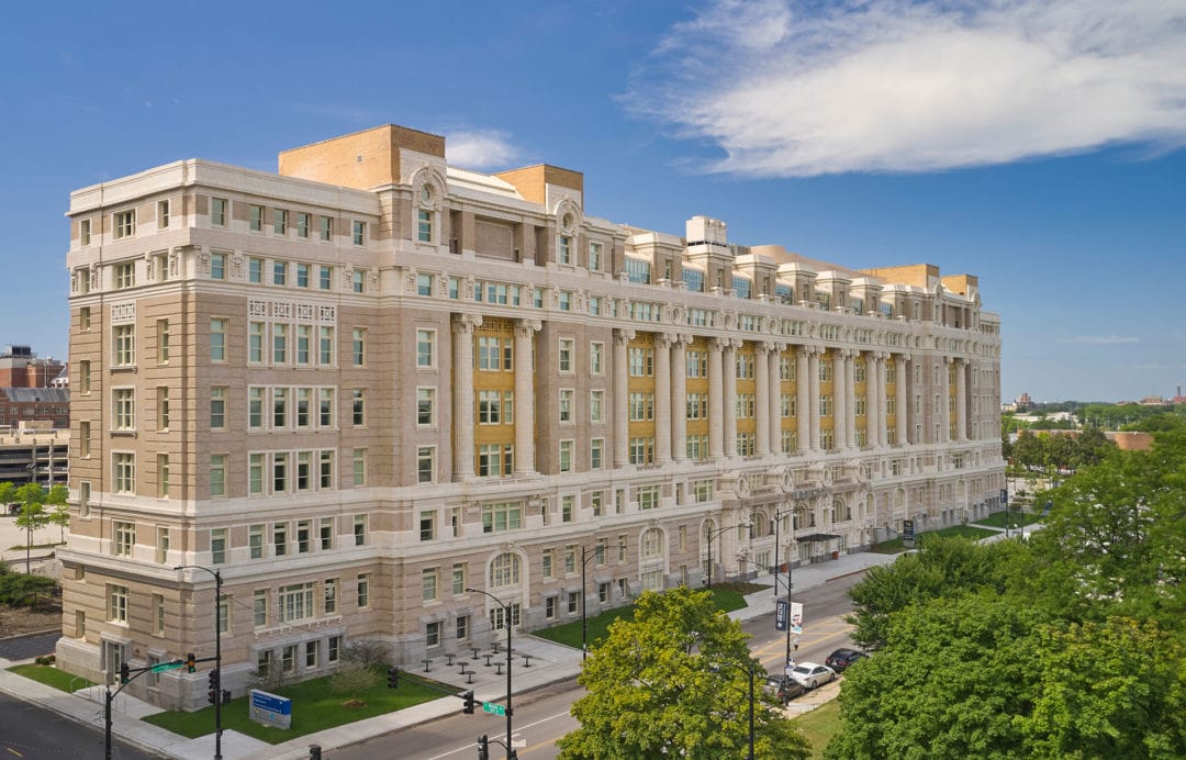 The bright exterior of the historic 1914 Beaux-Arts building after its renovation, surrounded by greenery. 
