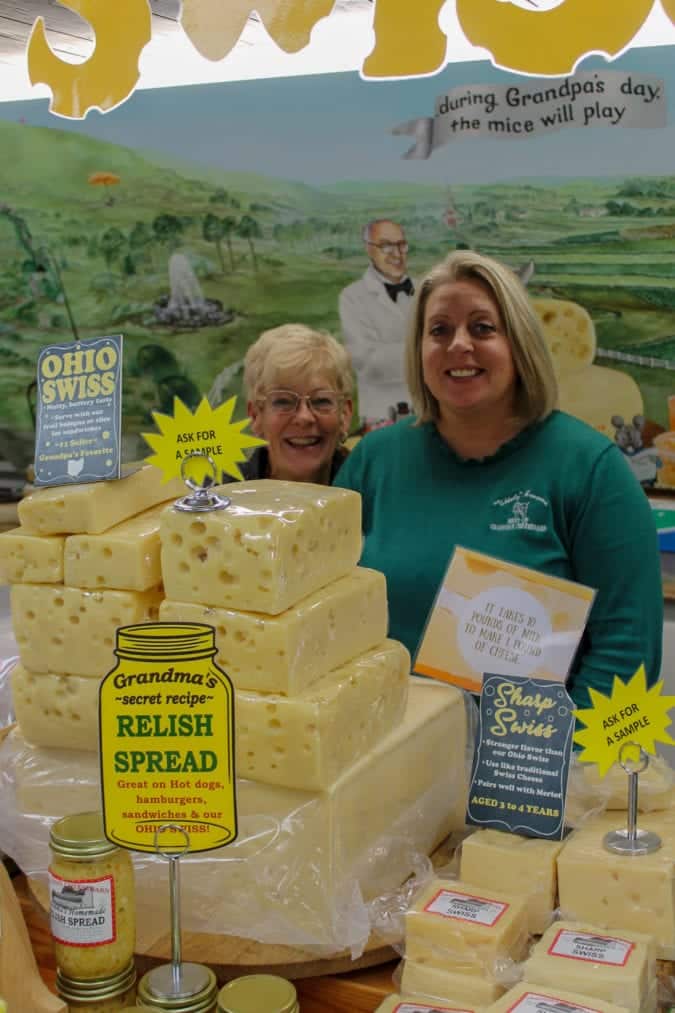 Vera Baum and Mistie Poorbaugh behind several stacks of cheese.