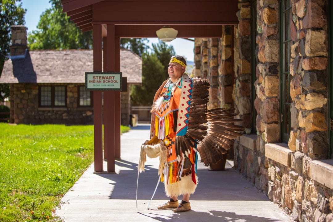 A native american man is dressed in a festive headdress and fringe ready for a powwo