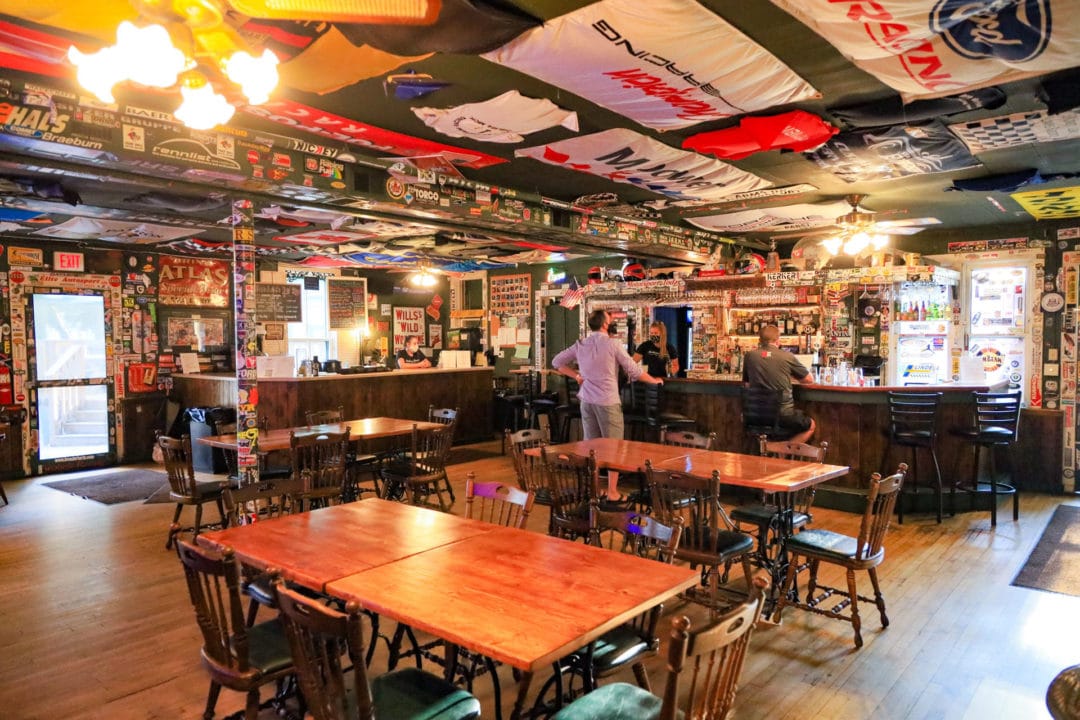 The inside of a mostly empty tavern with walls and ceiling decorated with road racing signs and paraphernalia