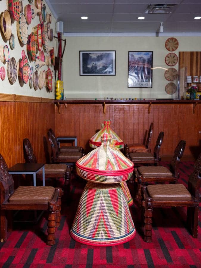 Line of decorative wooden chairs lined up on red and black patterned carpet with standing colorful woven baskets standing in between chairs