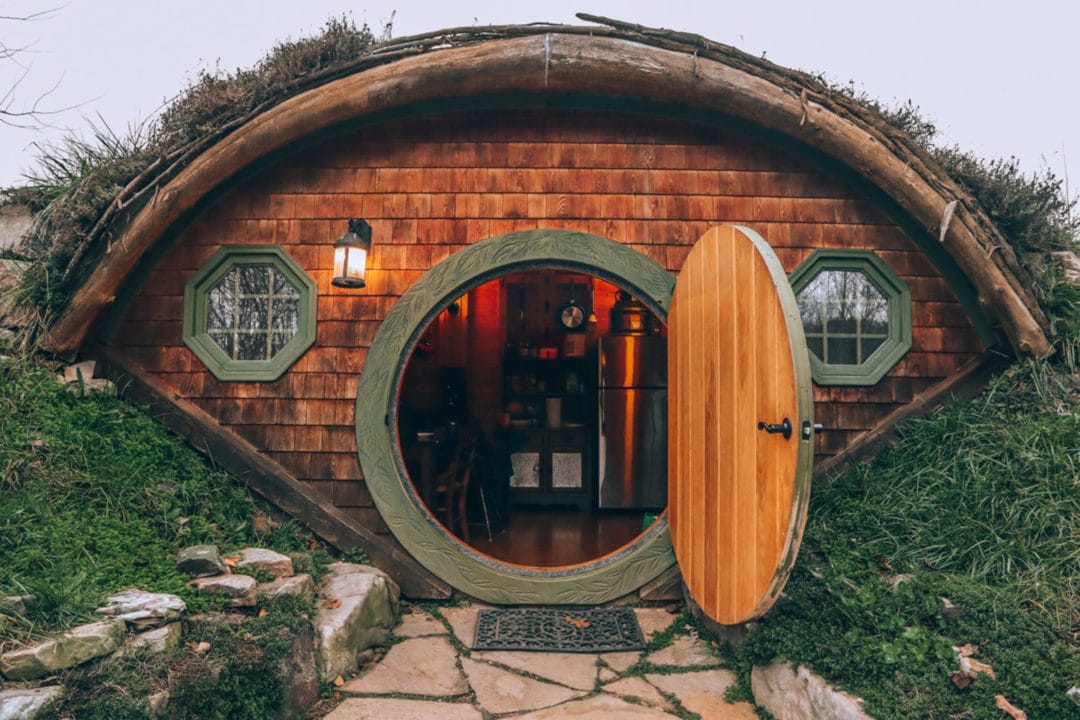 a wood shingled hut half buried in a hillshide with the door open and a kitchen visible inside