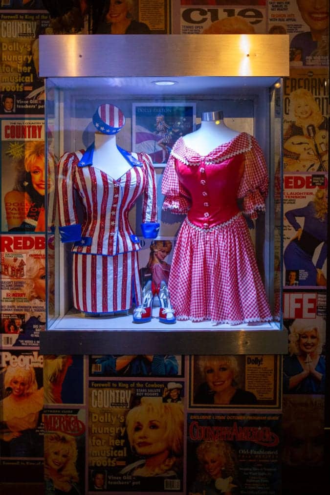 a display case containing two of dolly parton's costumes including a stars and strips outfit and a red gingham dress