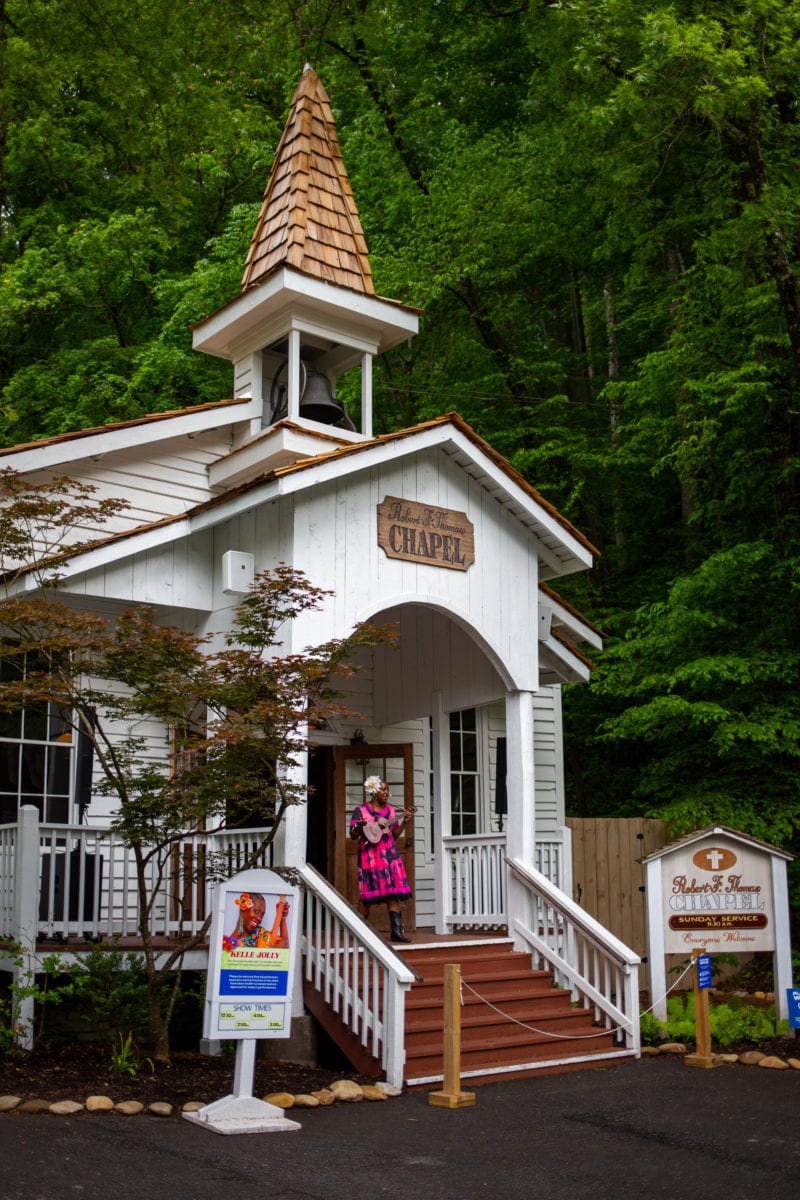 a black woman plays the ukulele on the steps of a white chapel