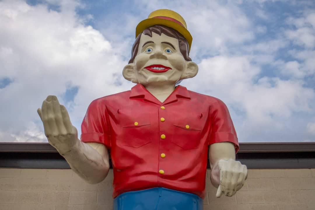 a muffler man wears a red shirt, blue pants and a yellow hat