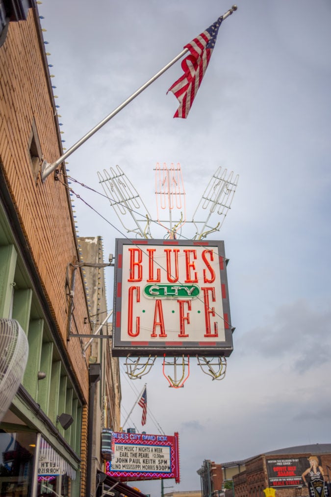 A neon sign featuring three oversized forks and the words "Blues City Cafe"