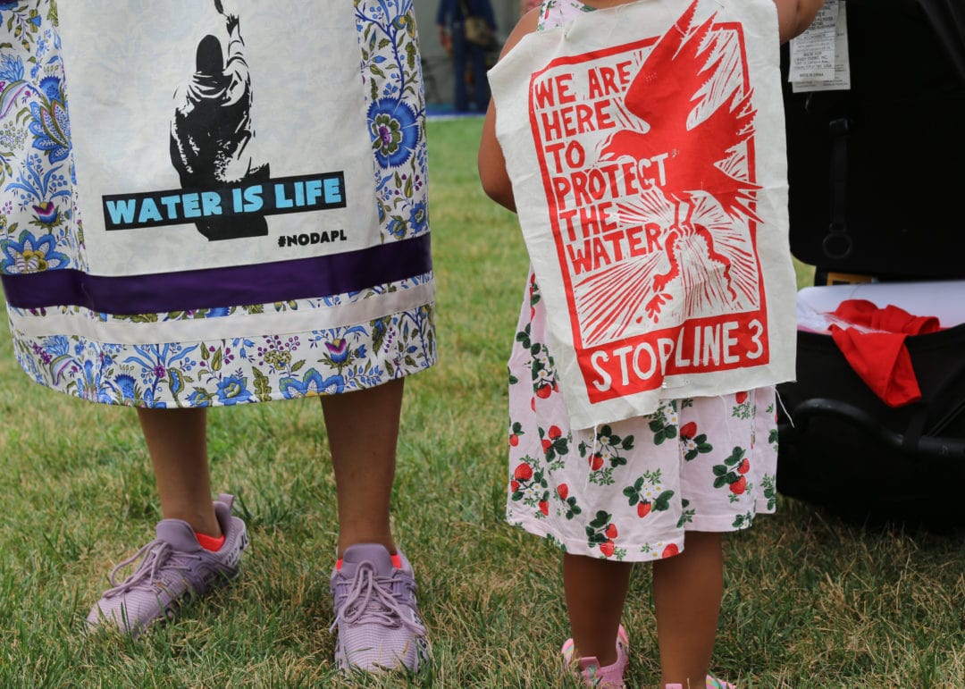 a woman and child wear pieces of cloth that say "we are here to protect the water" and "water is life"