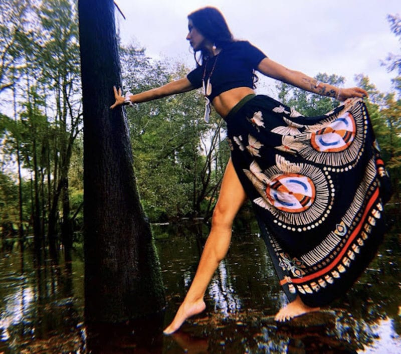 Woman walking in water and posing with a tree in native dress
