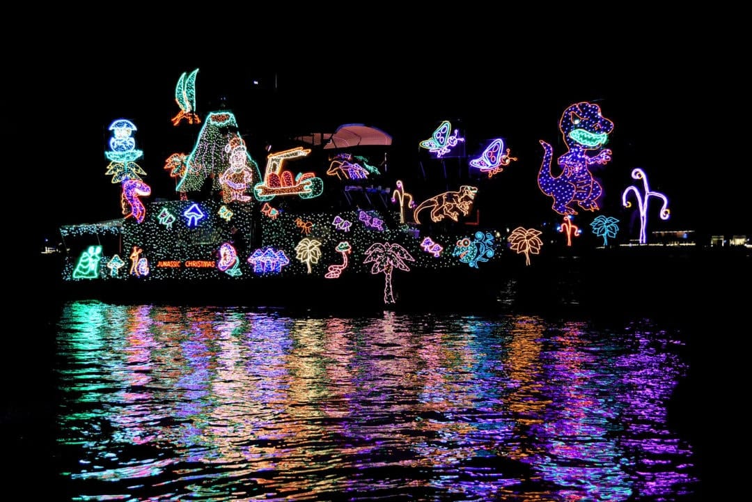 A boat decked out in holiday lights floating on the water in the dark