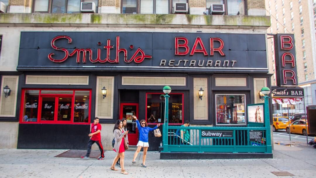 pedestrians stand outside of smith's bar and restaurant located next to a subway entrance
