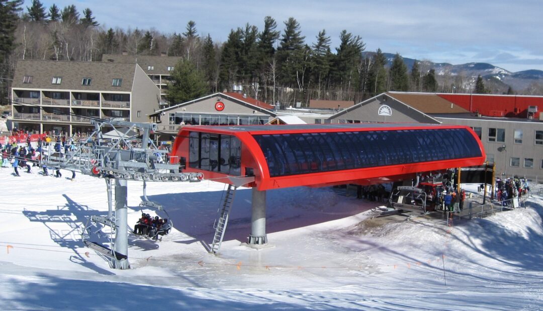 a snowy ski resort with a red ski lift outbuilding surrounded by pine trees and blue skies