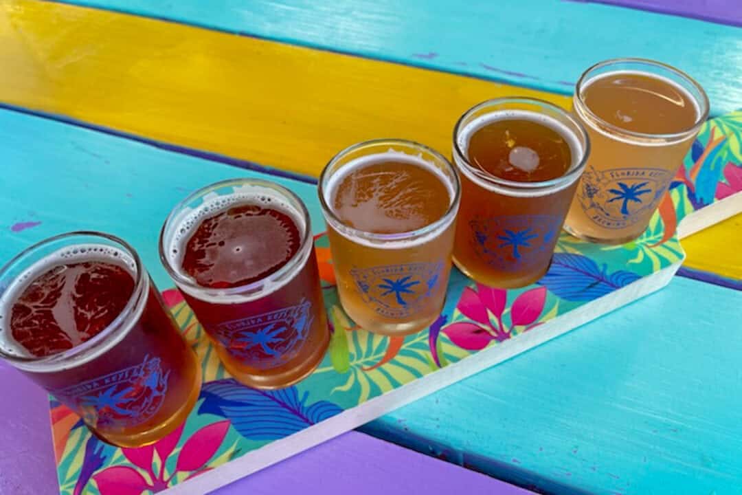 a flight of five beers set on a wooden picnic table painted bright colors