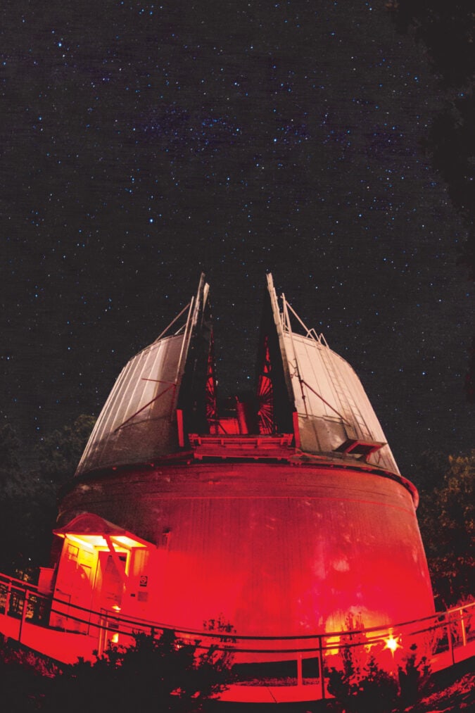 a large domed observatory lit by red lights under a night sky full of stars