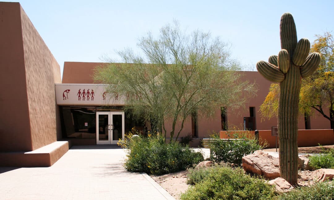 the entrance to an orange concrete museum with cacti out front