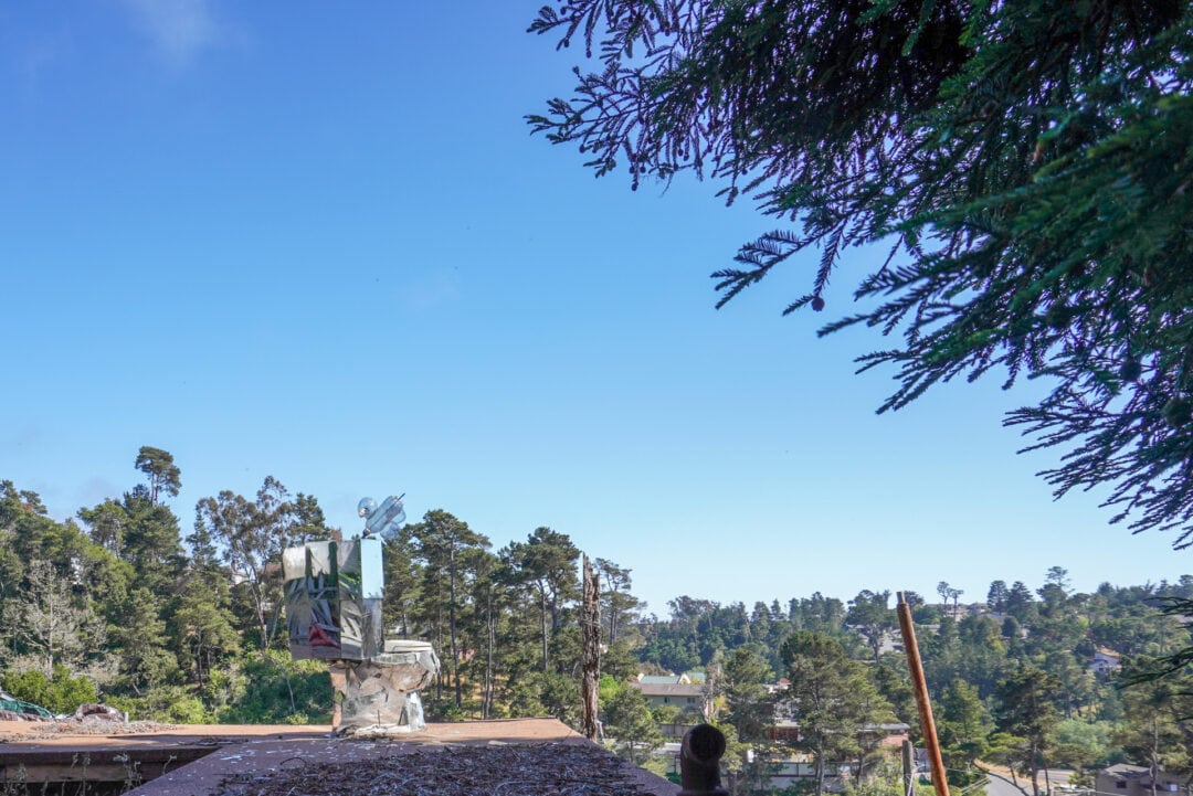 A toilet covered in mirrors sits on top of a roof against a blue sky