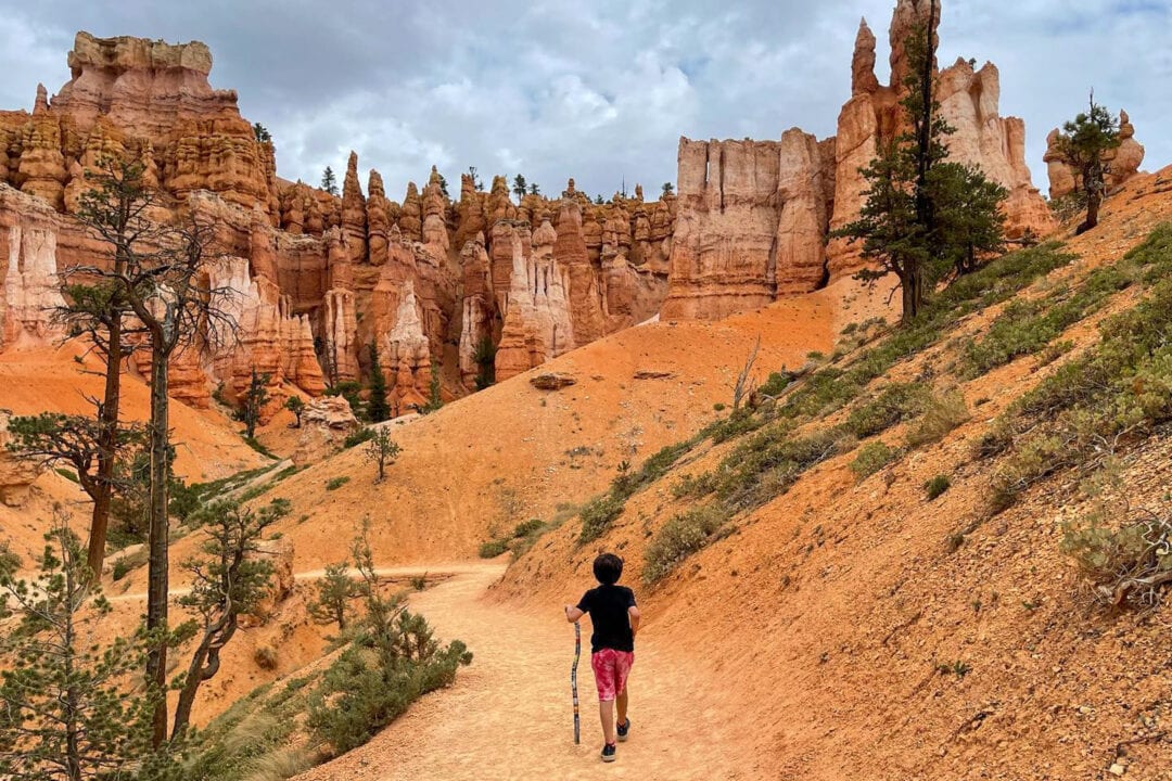 a kid uses a walking stick while hiking among red rock formations