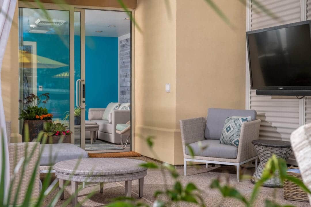 a room in a resort with a tv, grey furniture and a sliding glass door