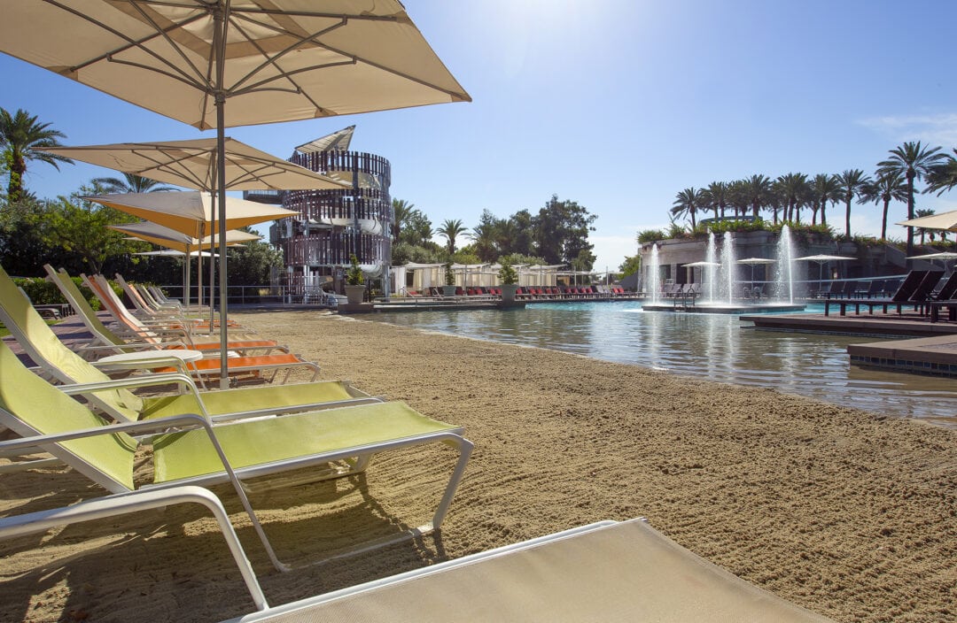 lounge chairs, umbrellas and palm trees line an outdoor pool
