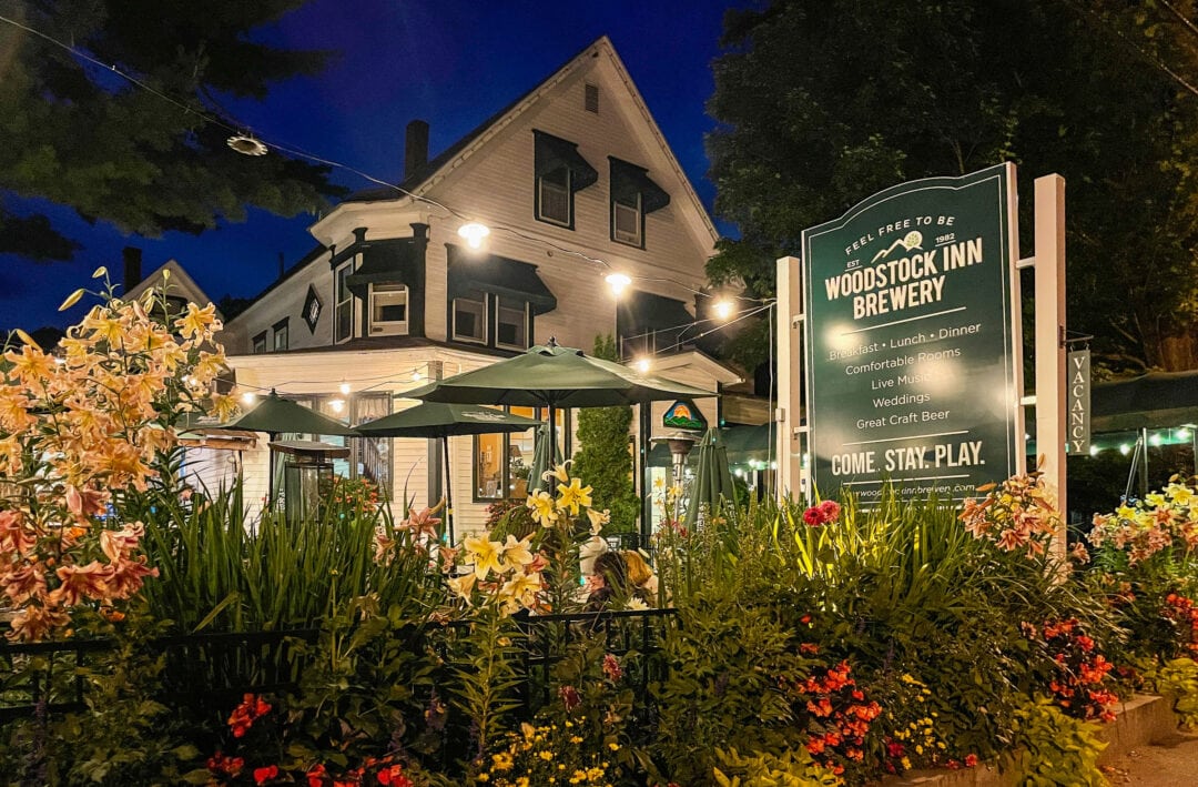 a white and green inn surrounded by colorful flowers at night, woodstock inn brewery