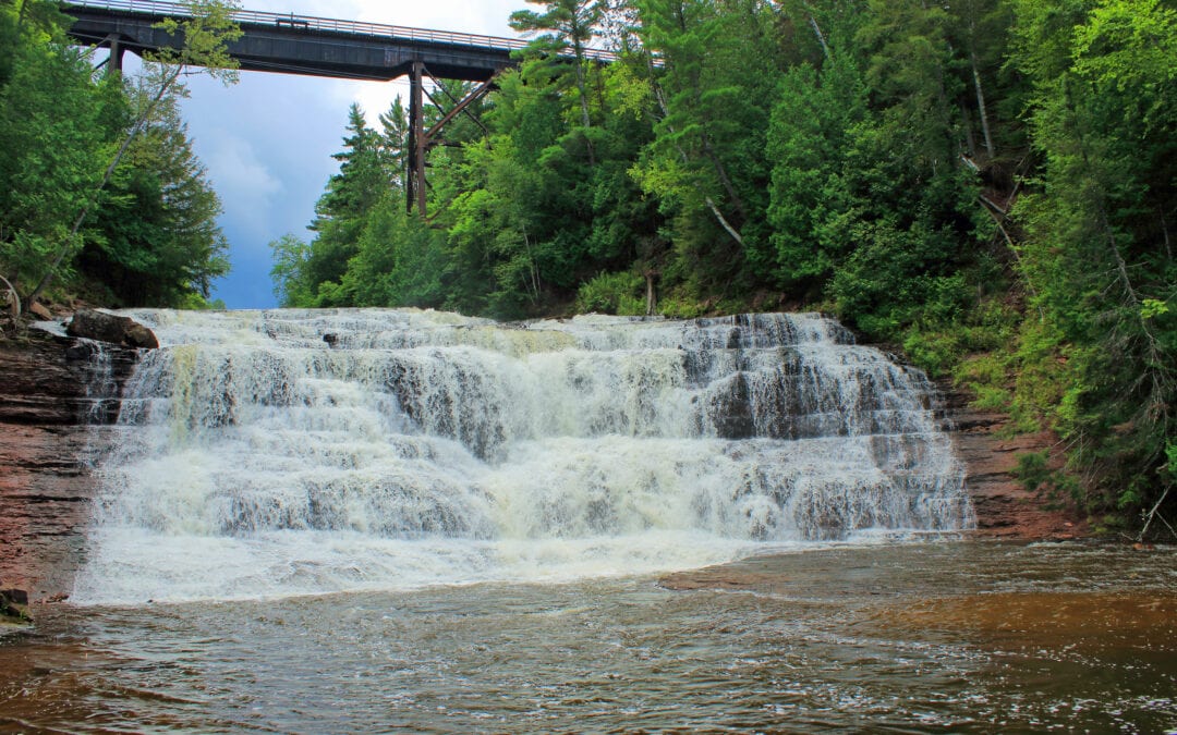 a short waterfalls cascades over rocks surrounded by greenery