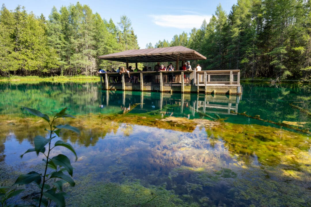 people stand on a wooden deck in the middle of a clear body of water kitch-iti-kipi