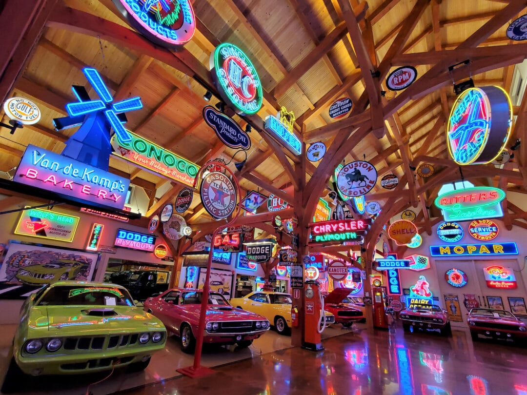 A view from inside a barn-like structure full of neon signs and vintage cars