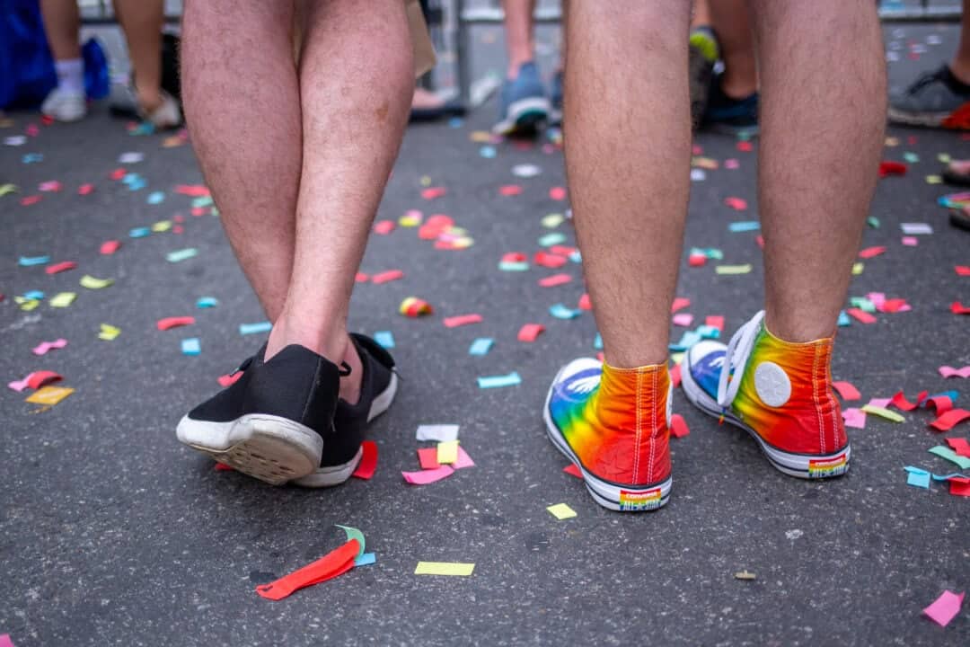 a pair of legs, one with black shoes and one with a pair of rainbow hightops