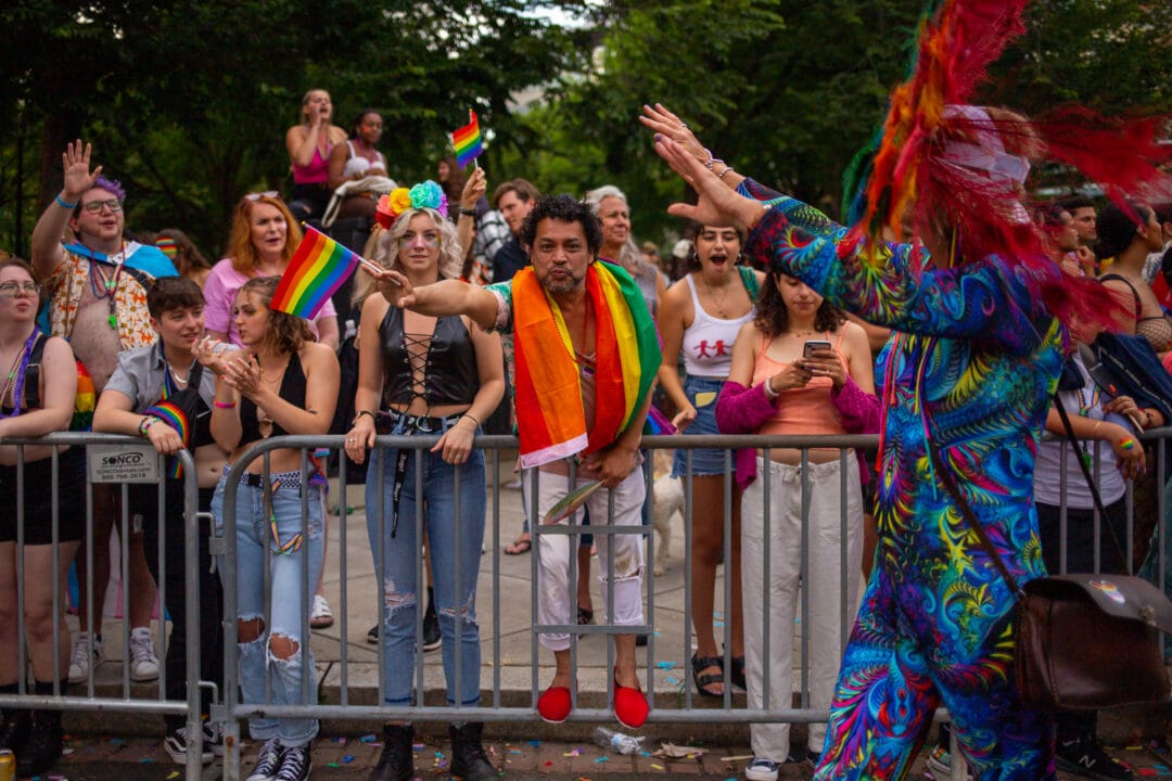 a crowd of colorful spectators watches a pride parade