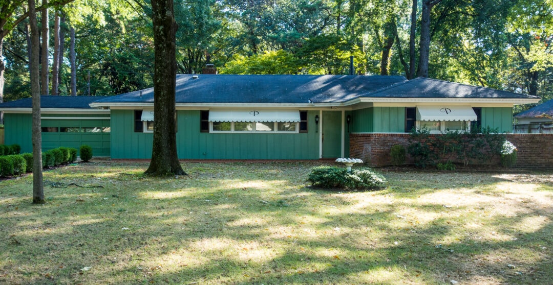 a one-story house painted green with white awnings featuring a green P