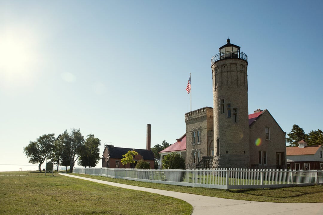 a grey stone lighthouse stands next to the shore against a clear blue sky