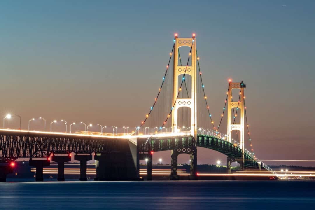a long suspension bridge over water is lit up at night