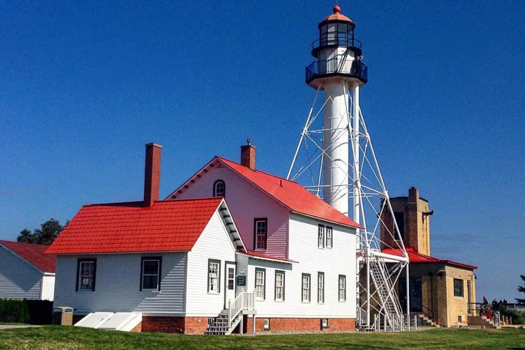 a white house with a red roof next to a light set against a blue sky