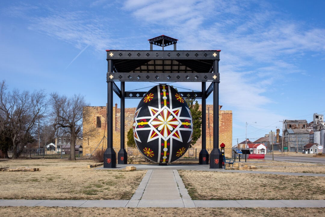a large black, white, red and yellow painted czech egg stands under a black pavilion