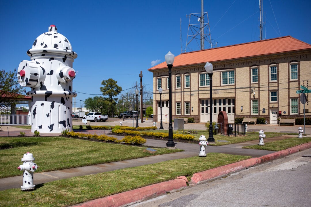 an oversized black and white spotted fire hydrant stands outside of a beige brick building