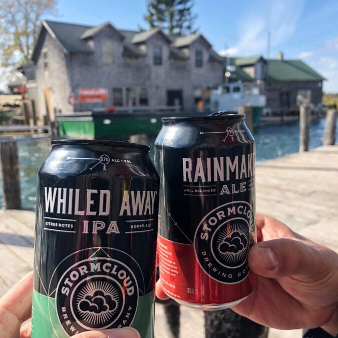 two hands cheers two cans of beer on a dock