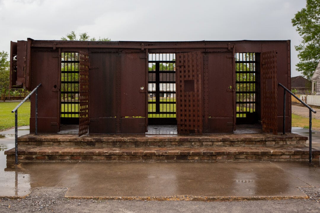 a large rusty metal slave pen displayed outside on a brick platform