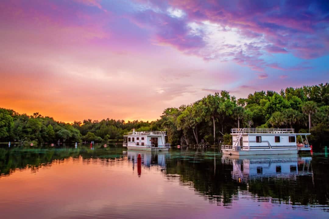 a marina with floating houses under a pink and purple sky at sunset