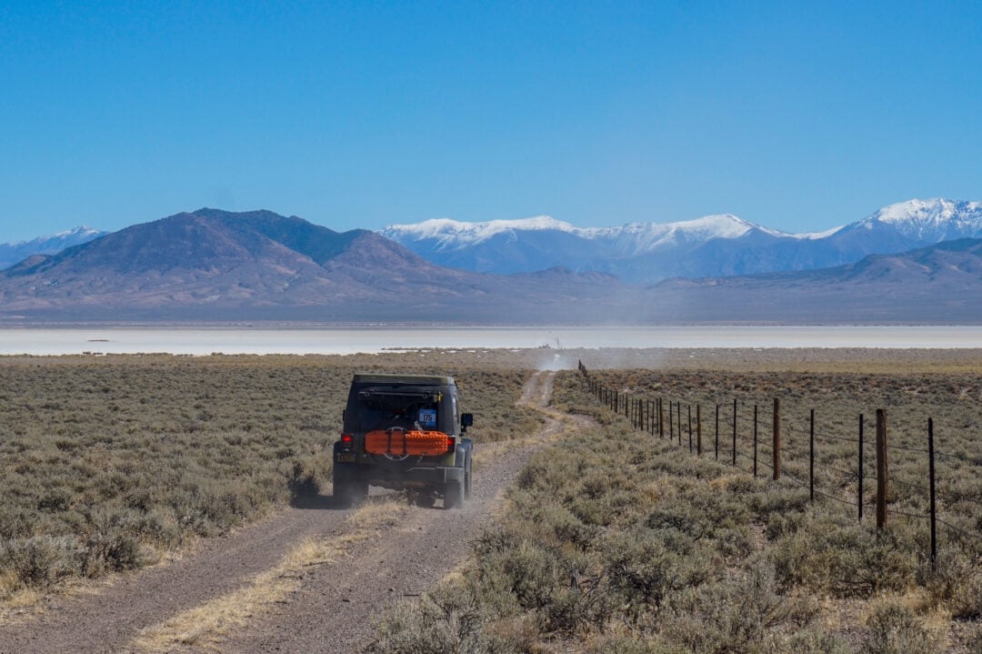An off-road vehicle traveling down a dirt road with snow-capped mountain peaks in the background