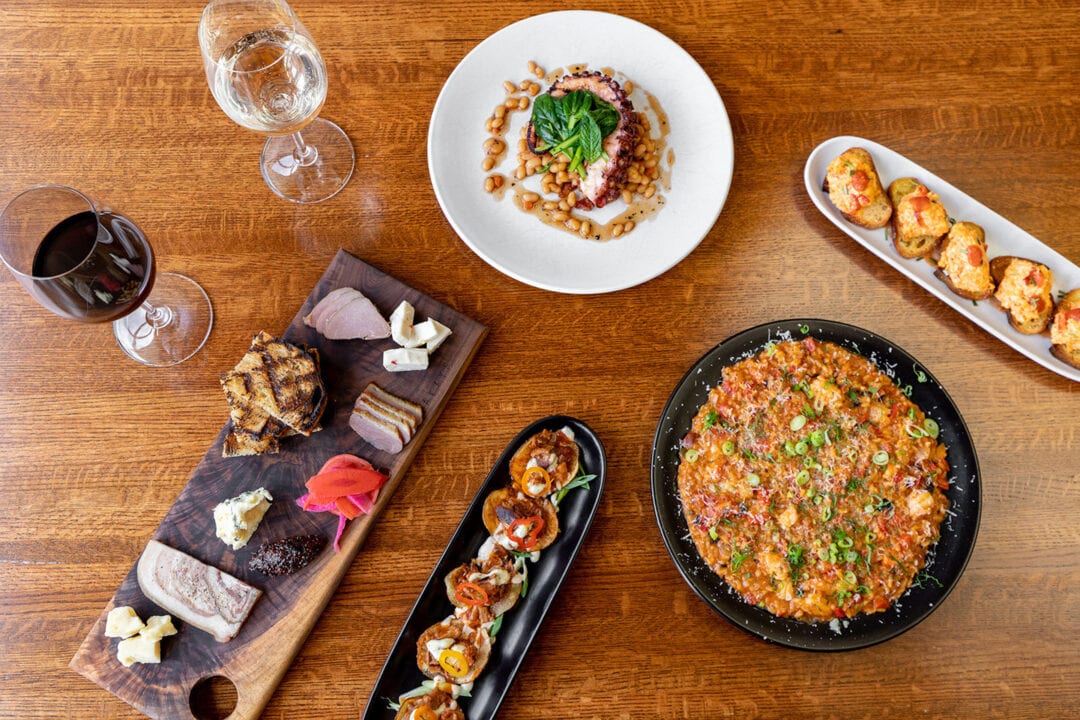Small plate food offerings sit on a table along an assortment of wine glasses.