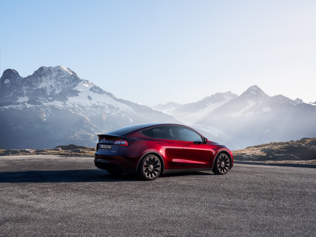 A sleek red car sits in front of a hazy mountain range.