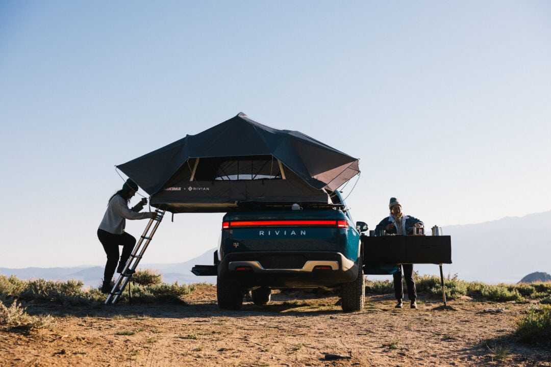 A traveler climbs a ladder up to a tent on the roof of a car.