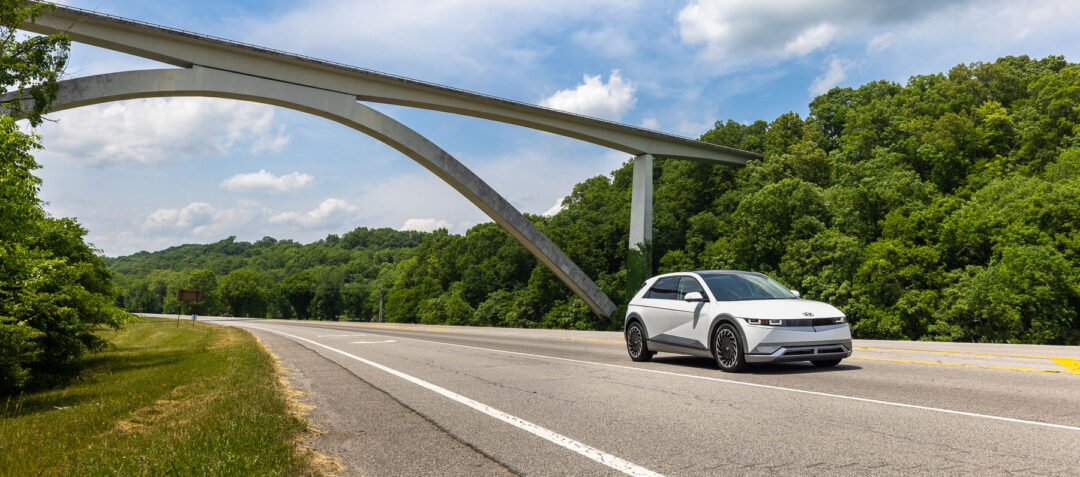 A crossover vehicle drives beneath an arched bridge.