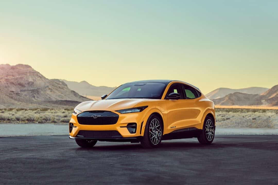 A shining yellow car stands alone with dramatic rock features in the background.